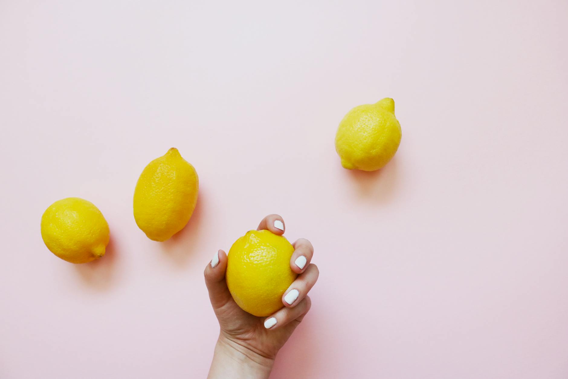 A hand holding a fresh lemon on a soft pink background, symbolizing the simplicity of clitoral pleasure with a lemon vibrator.
