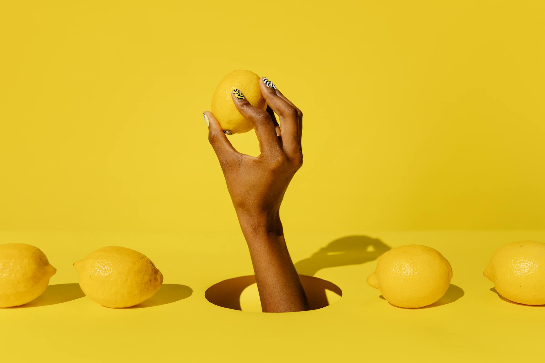 A hand holding a fresh lemon against a vivid yellow background, symbolizing the bright and refreshing design of lemon vibrators