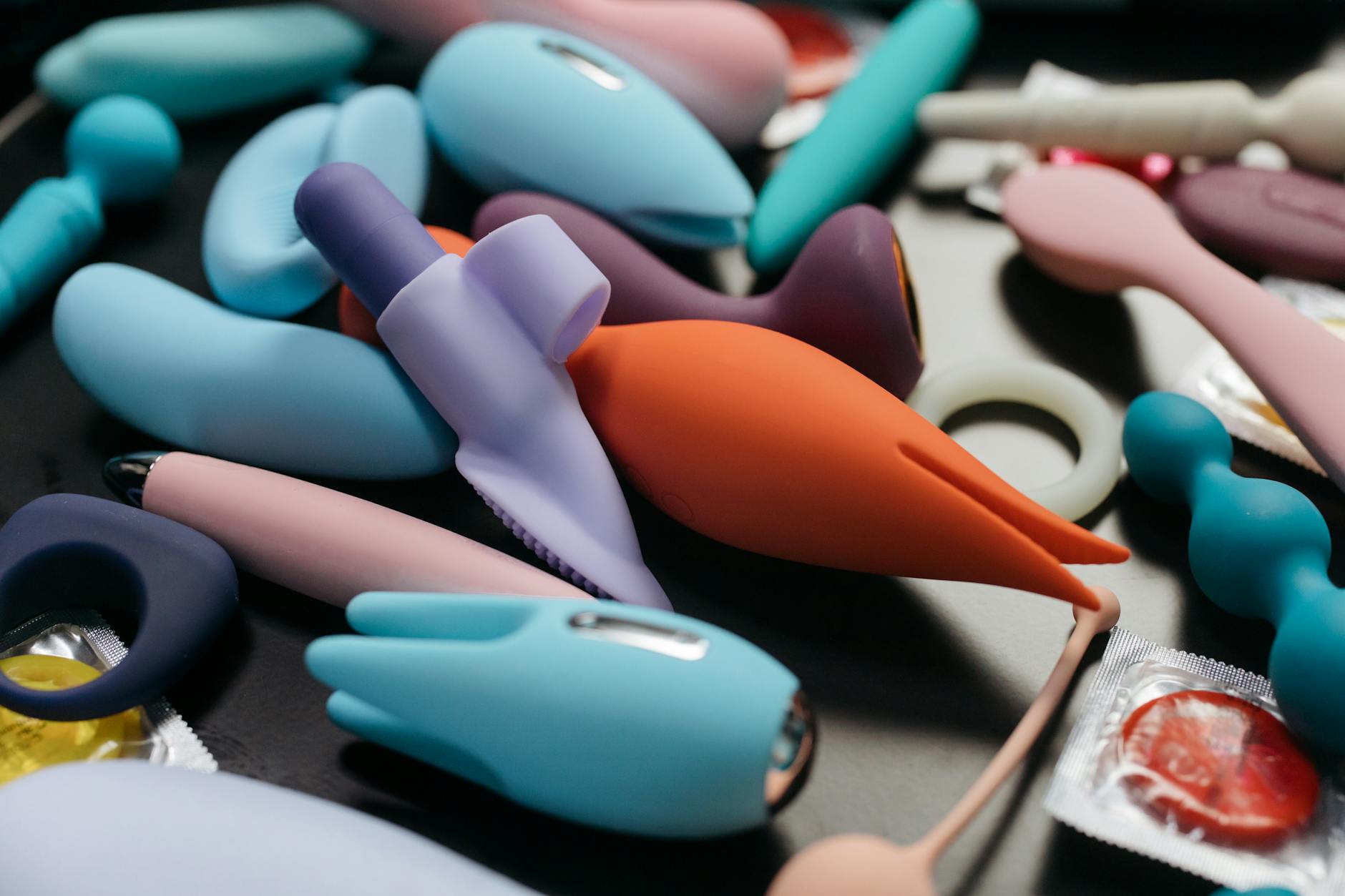 Zwei Hände halten rosa und blaue Silikonvibratoren gegen einen pastellfarbenen Hintergrund