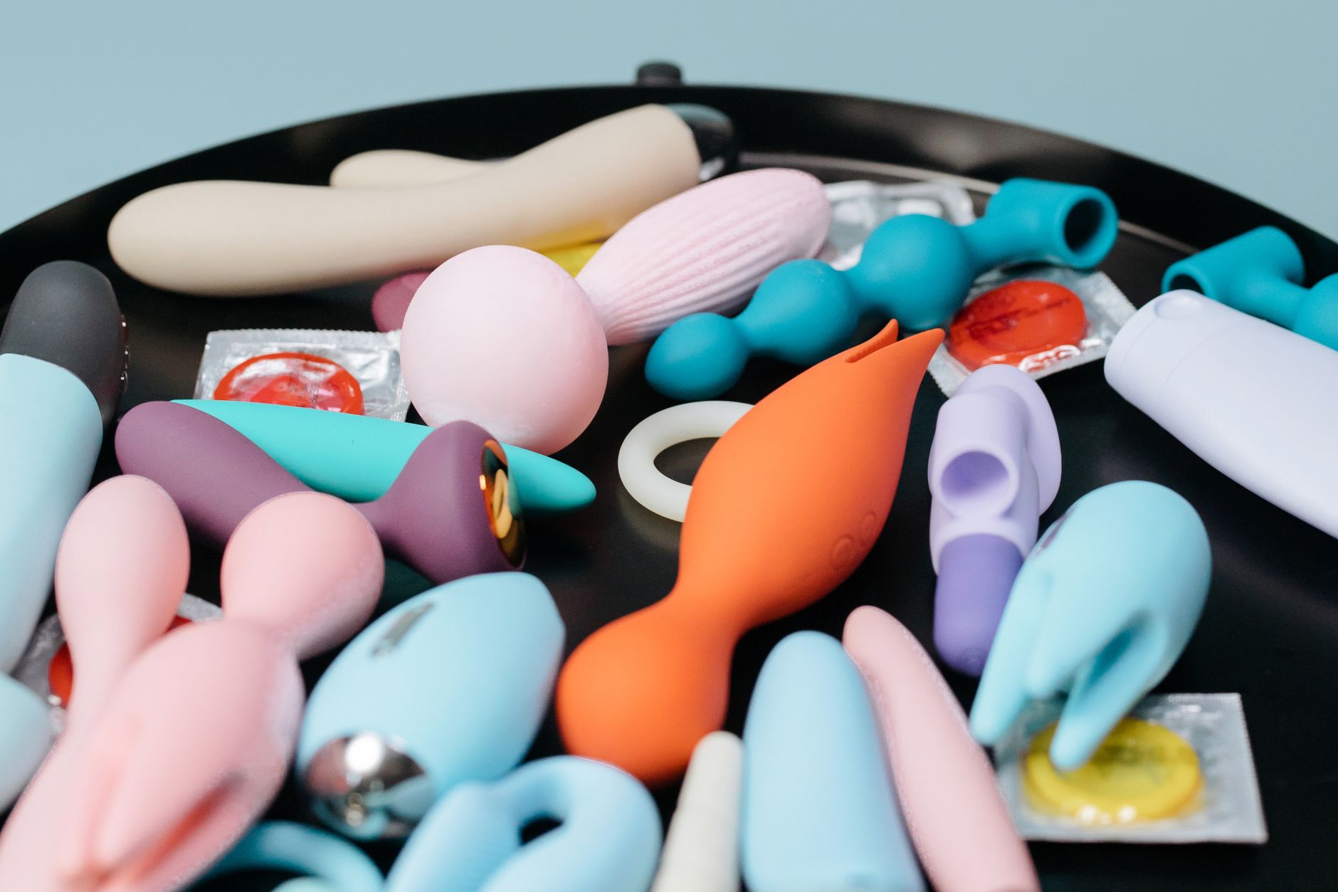 Eine Hand hält einen orangefarbenen Vibrator vor minimalistischem violettem Hintergrund und zeigt moderne Sinnlichkeit