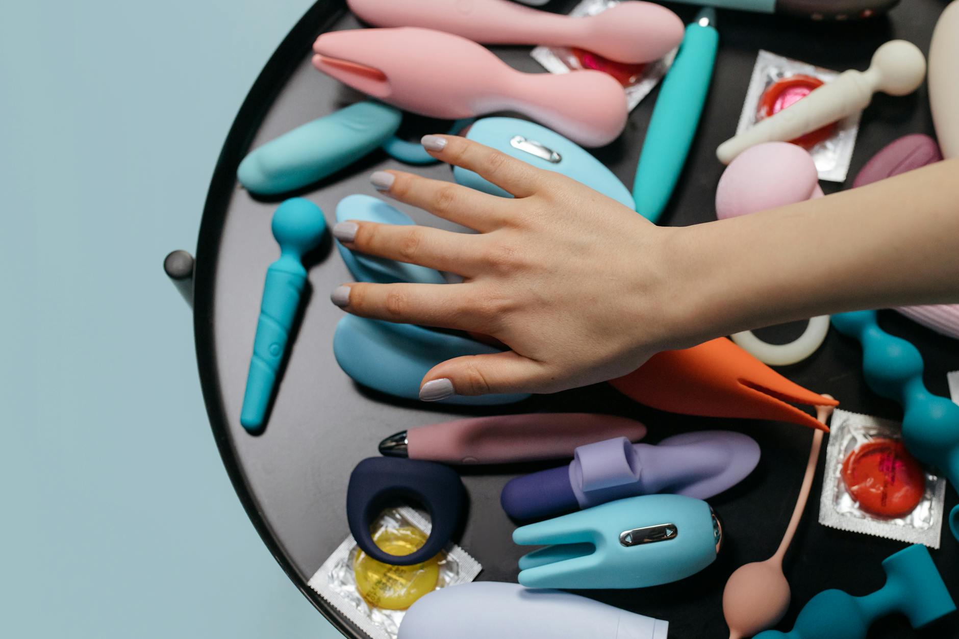 Woman holding pink and blue vibrators with contemplative expression, demonstrating intimacy and personal pleasure