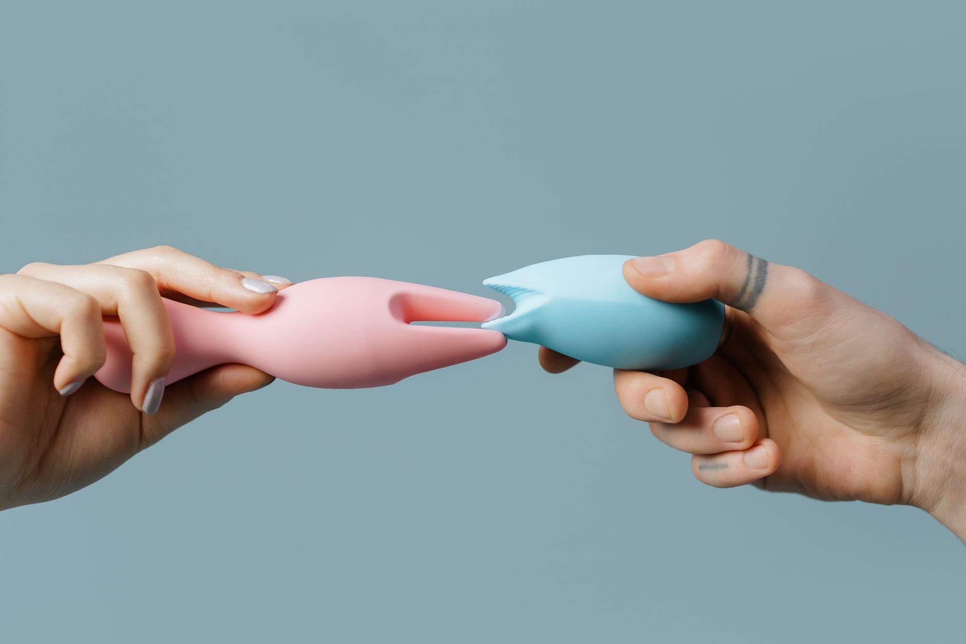Hands holding silicone vibrators together in intimate setting