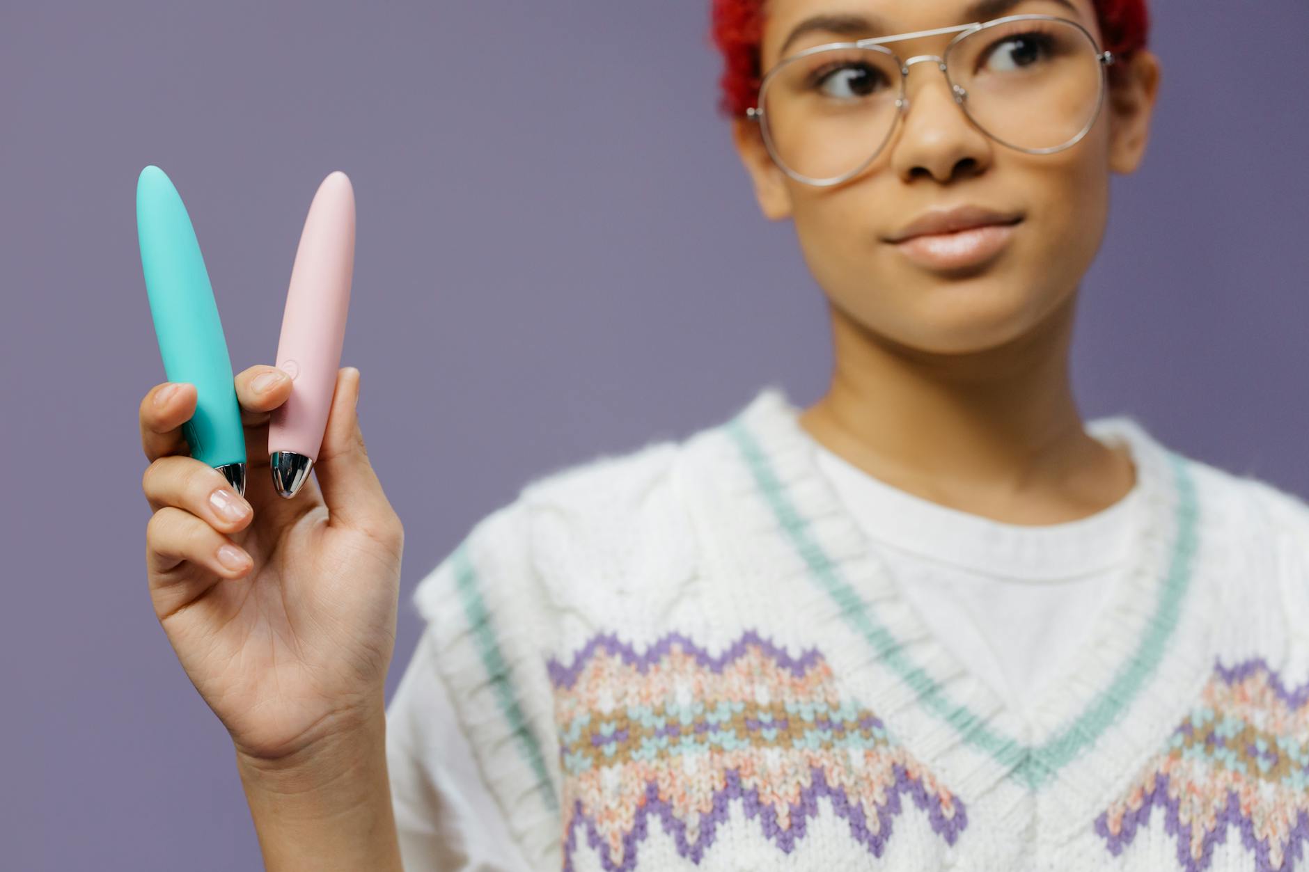 Two colorful clitoral vibrators held against a purple background