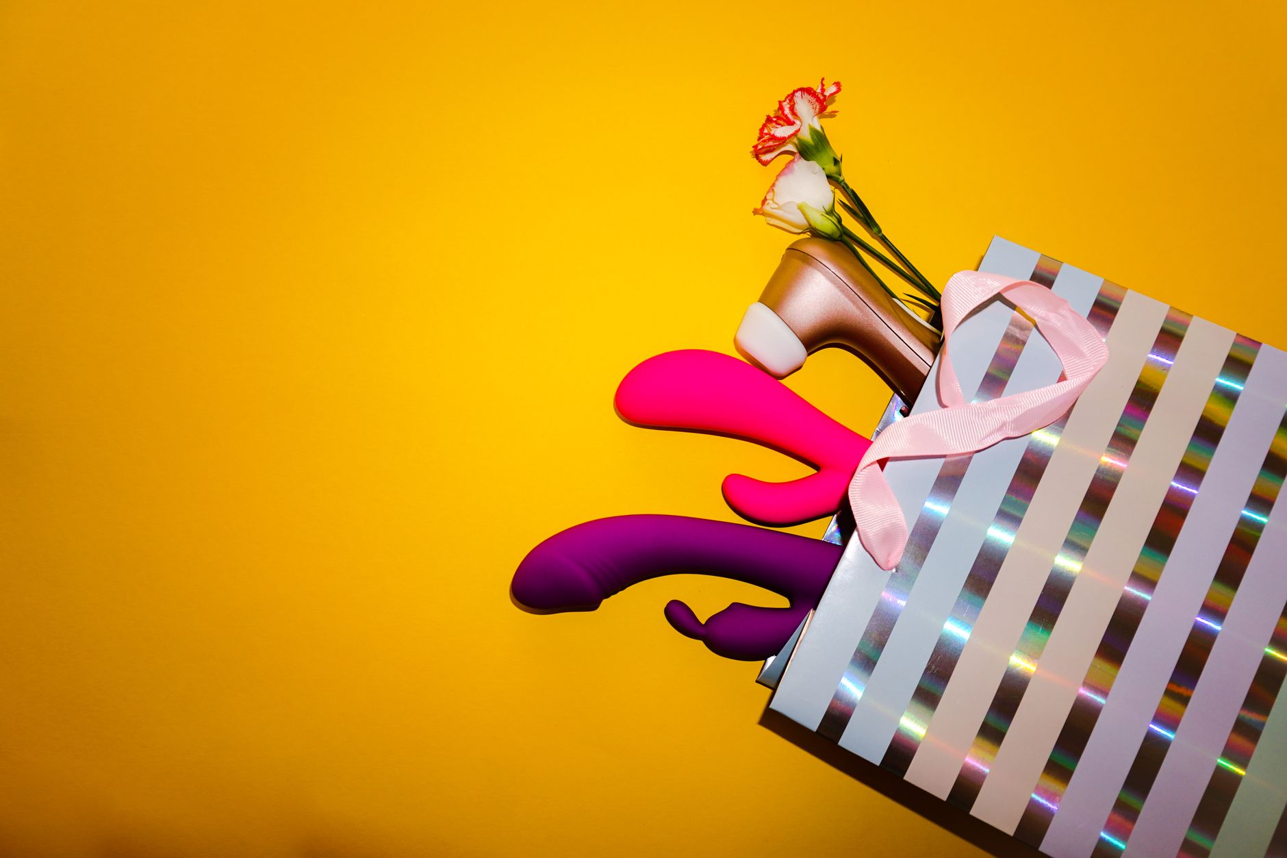 Bunte Vibratoren mit Blumen in einer holografischen Geschenktasche auf lebendigem gelbem Hintergrund