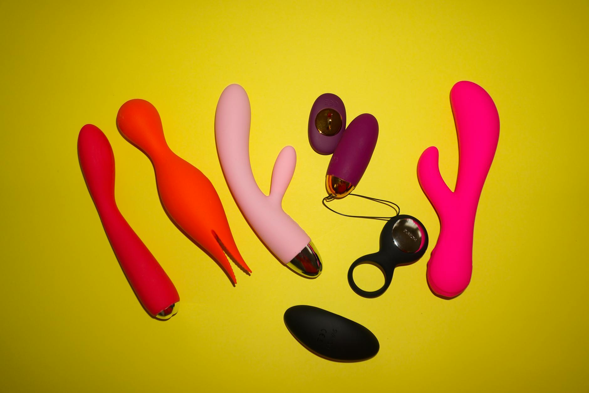 Bright studio display of colorful clitoral vibrators including lemon-shaped toys on a yellow background