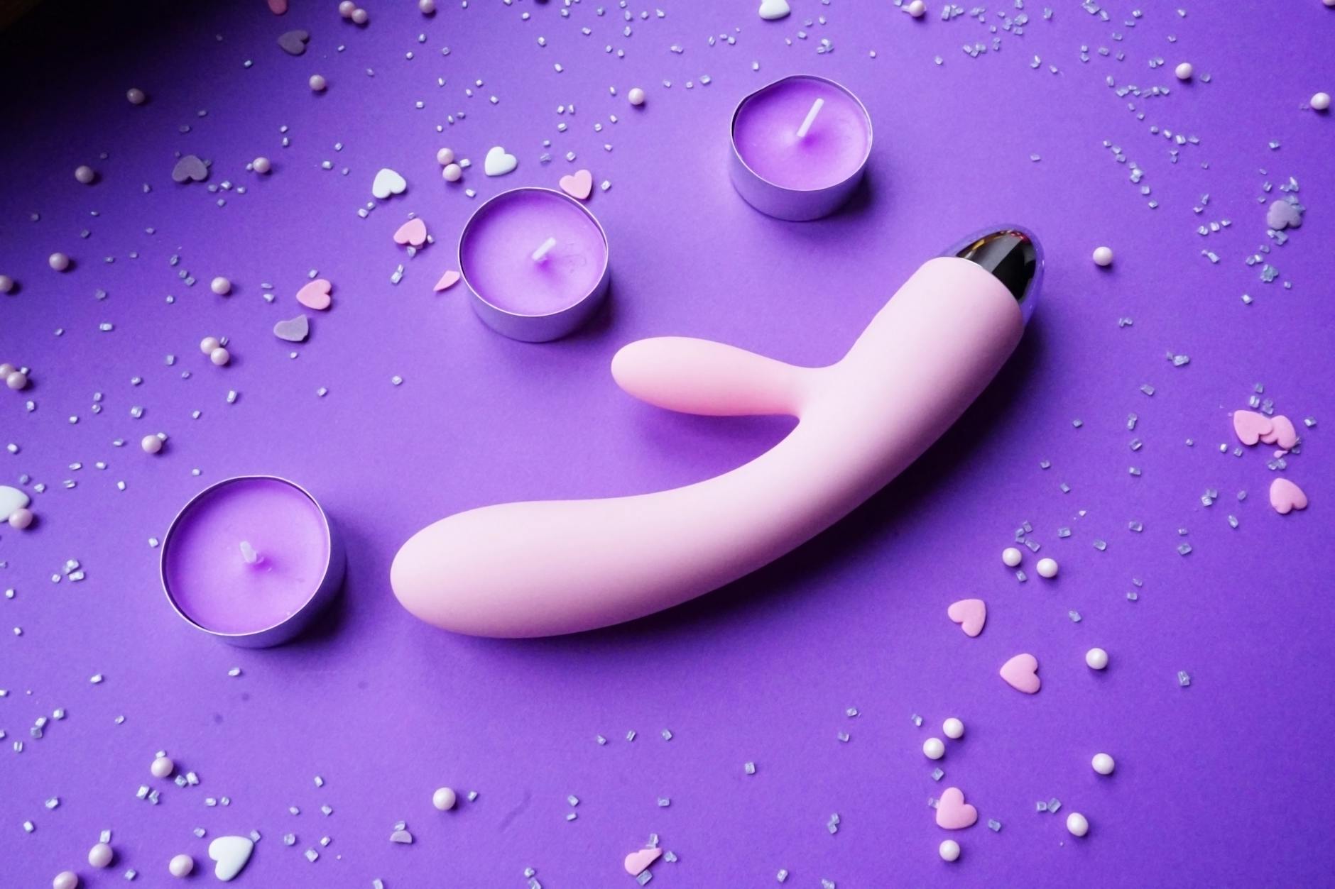 Rosafarbener Vibrator auf violettem Hintergrund mit Herzherzkonfetti und Kerzen für eine romantische Atmosphäre